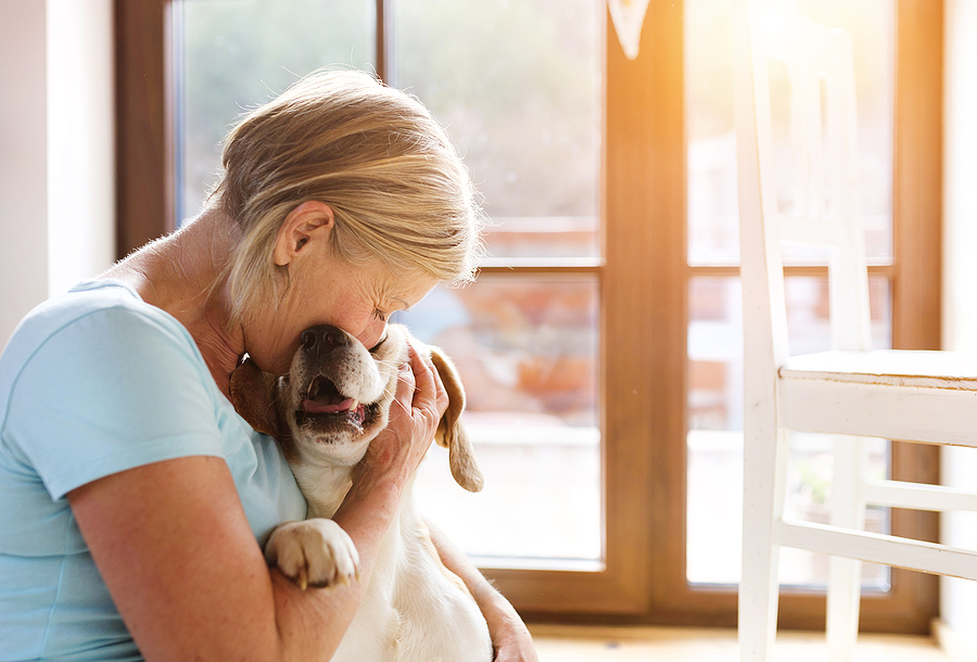 A senior woman snuggles a blonde lab inside her home.