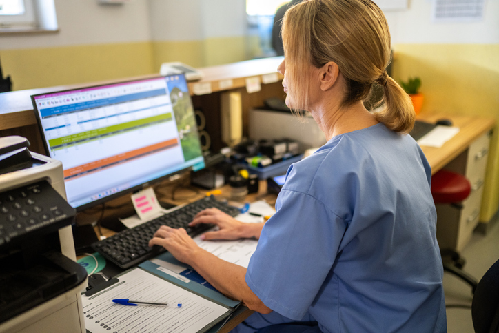 A focused woman in medical scrubs manages appointments at a vet station, surrounded by office essentials and a computer, providing administrative support in a pet care environment.