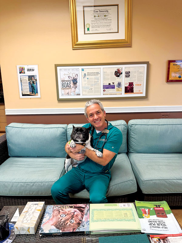 Veterinarian sits on a sofa holding a small dog.