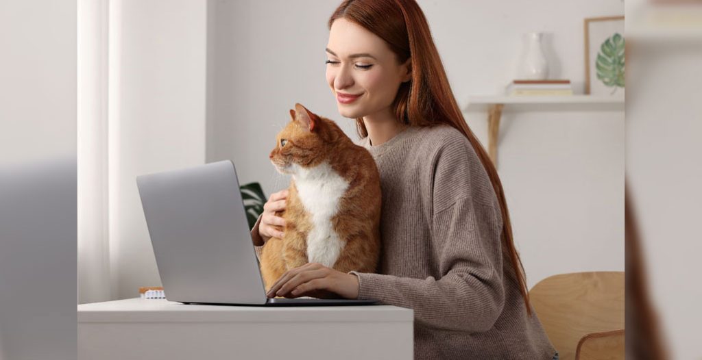 woman sits with cat while on a laptop