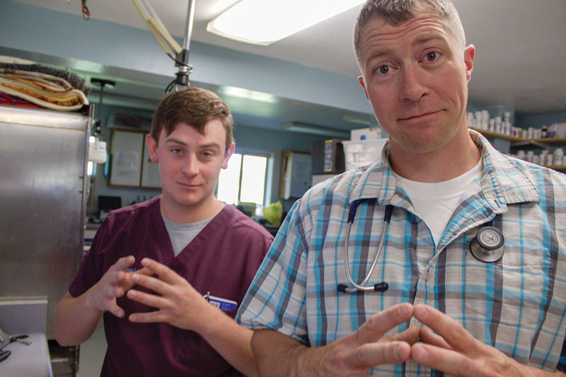 two men in a veterinary setting holding their hands up with their fingertips pressed together