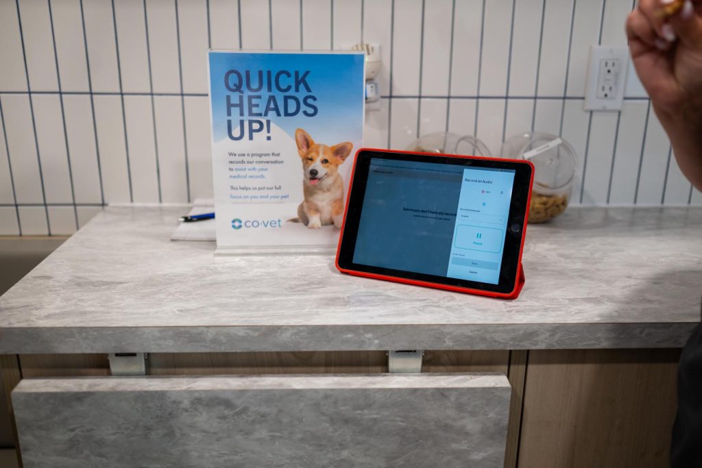 A tablet with a red case on a marble countertop displays an AI tool. Beside it is a sign with “Quick Heads Up!” and a dog image, set against a tiled wall.