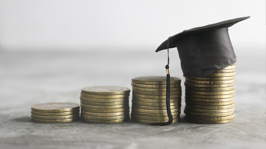 Graduation cap resting on the tallest of four increasing stacks of coins representing a grant.