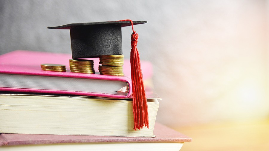 Graduation cap with a red tassel, gold coins, and stacked books against a softly blurred background.